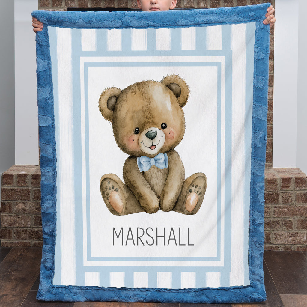 Child holding personalized minky teddy bear baby blanket with blue fur border by brick wall