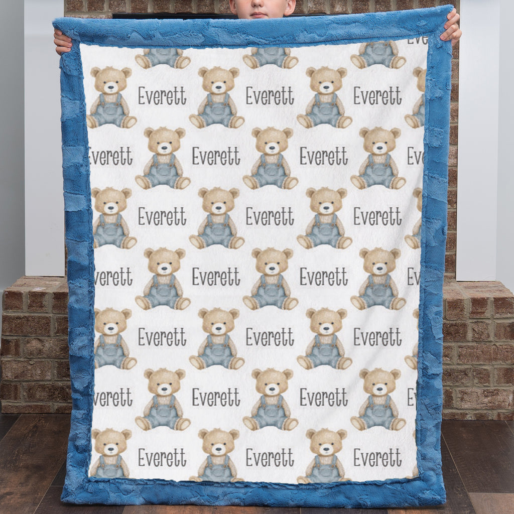 Personalized teddy bear minky baby blanket with blue fur border held up by brick fireplace