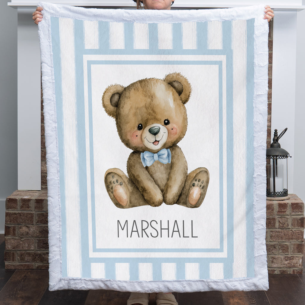 Personalized minky teddy bear baby blanket with blue stripe border held up by fireplace