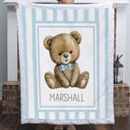 Personalized minky teddy bear baby blanket with blue stripe border held up by fireplace