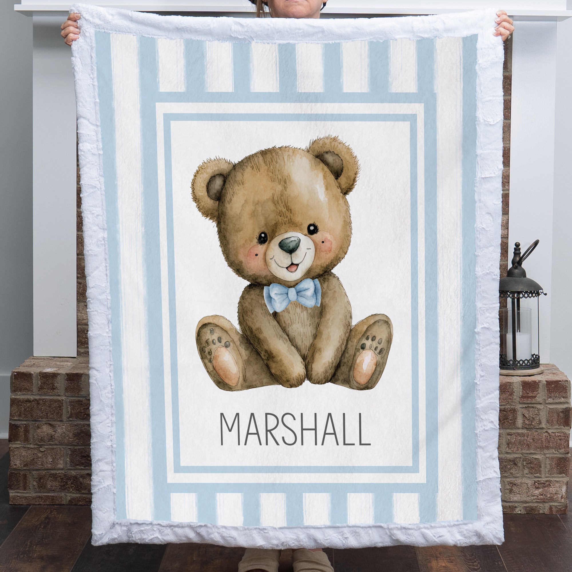 Personalized minky teddy bear baby blanket with blue stripe border held up by fireplace