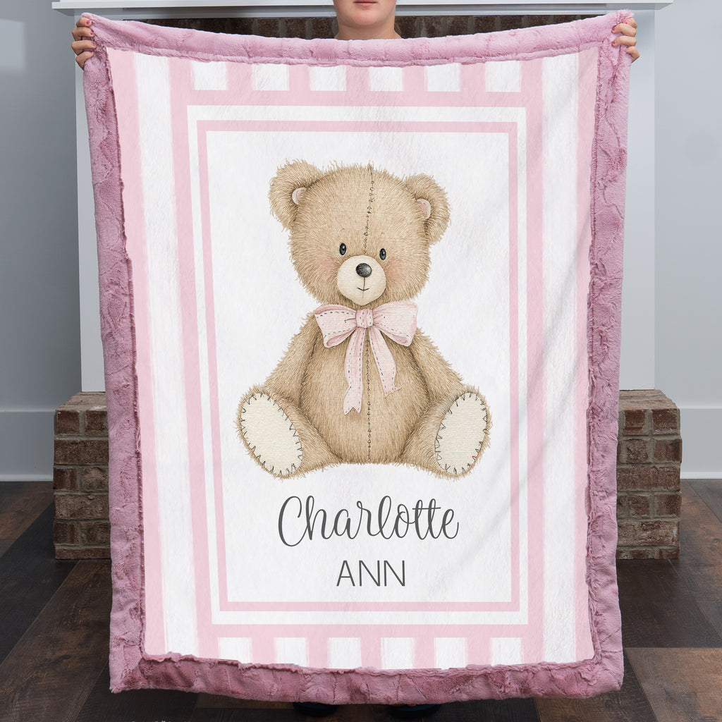 Personalized minky teddy bear baby blanket with deep pink fur border held up by fireplace