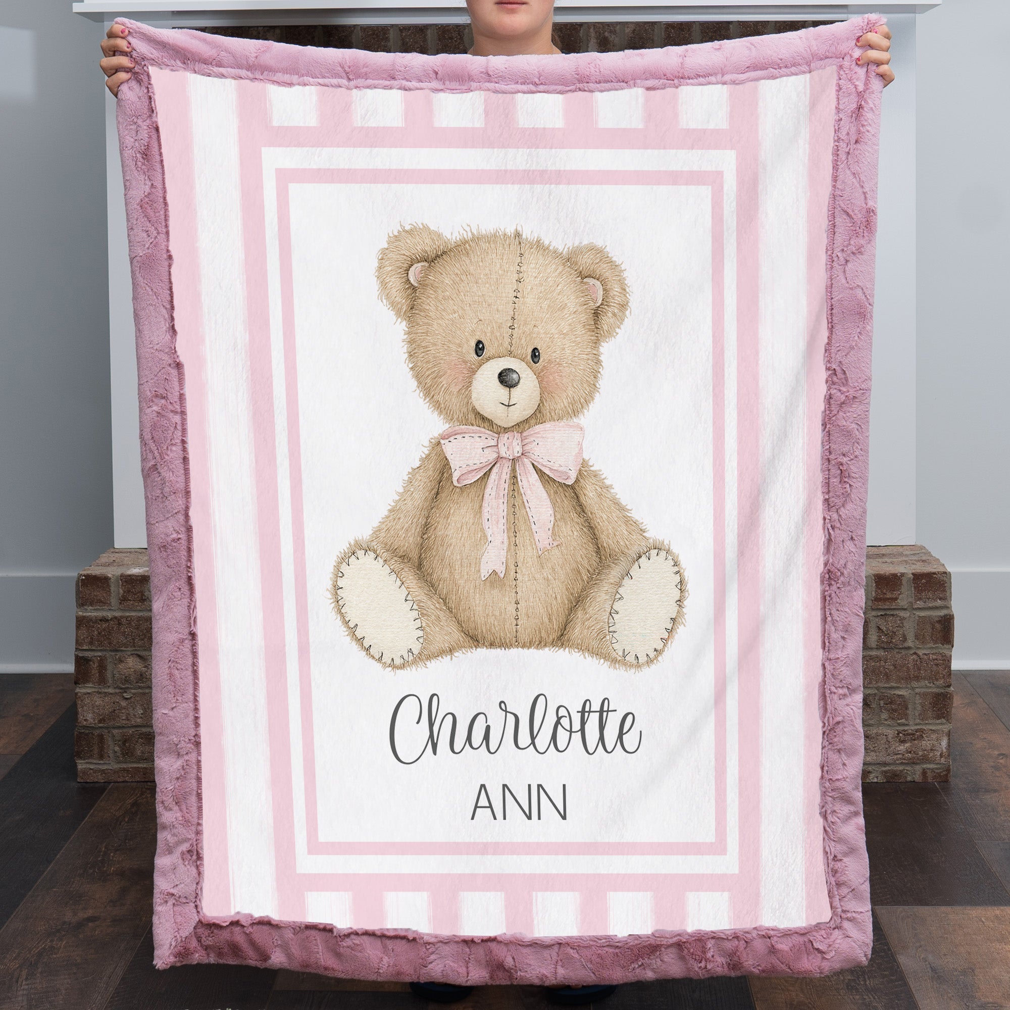 Personalized minky teddy bear baby blanket with deep pink fur border held up by fireplace