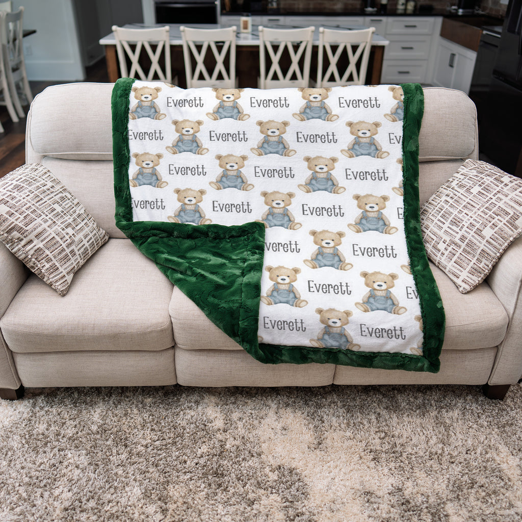 Personalized teddy bear minky baby blanket with green fur border draped over couch, minky back showing