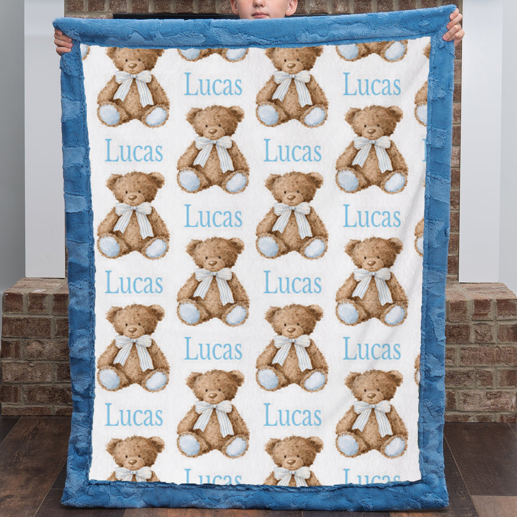 Personalized minky baby blanket with teddy bear print held up by child, blue trim close-up
