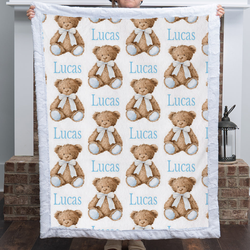 Personalized minky baby blanket with teddy bear print held up to show full pattern by fireplace