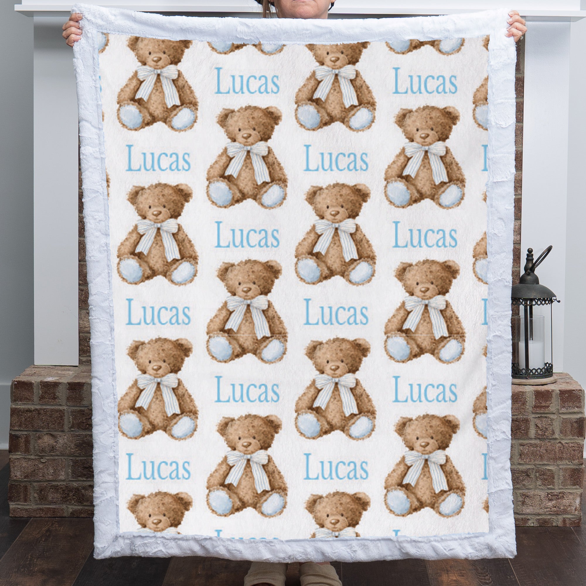 Personalized minky baby blanket with teddy bear print held up to show full pattern by fireplace