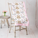 Personalized teddy bear minky baby blanket with pink border draped over rustic chair