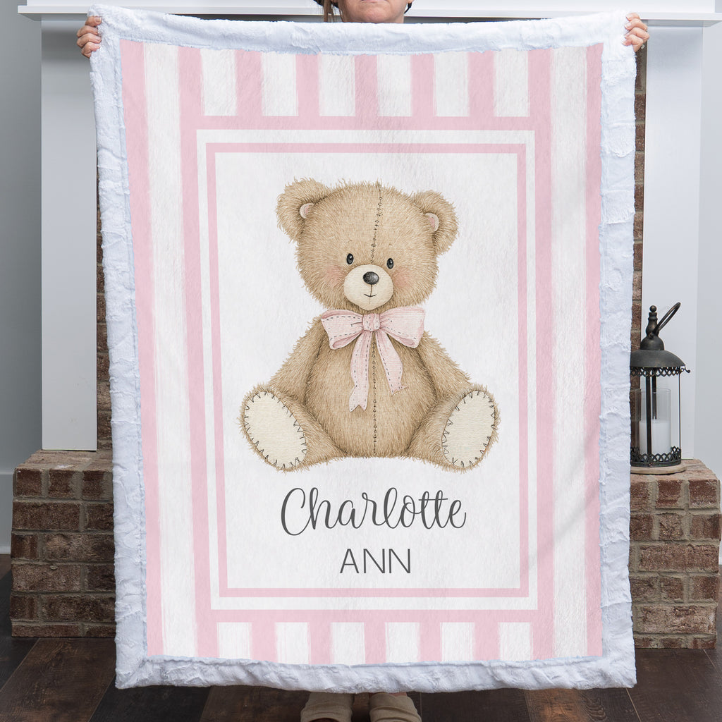Personalized minky teddy bear baby blanket with pink stripe border held up by fireplace