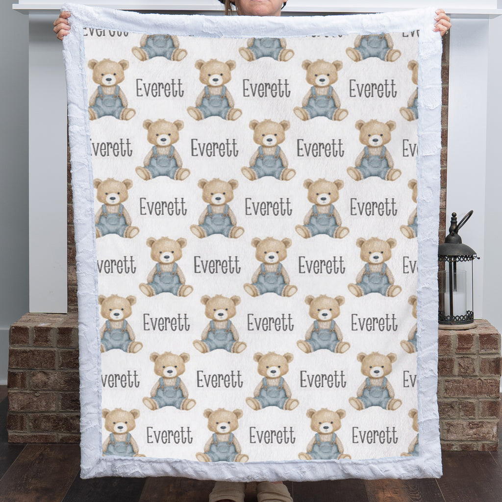 Personalized teddy bear minky baby blanket with white fur border held up by fireplace with lantern