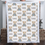 Personalized teddy bear minky baby blanket with white fur border held up by fireplace with lantern