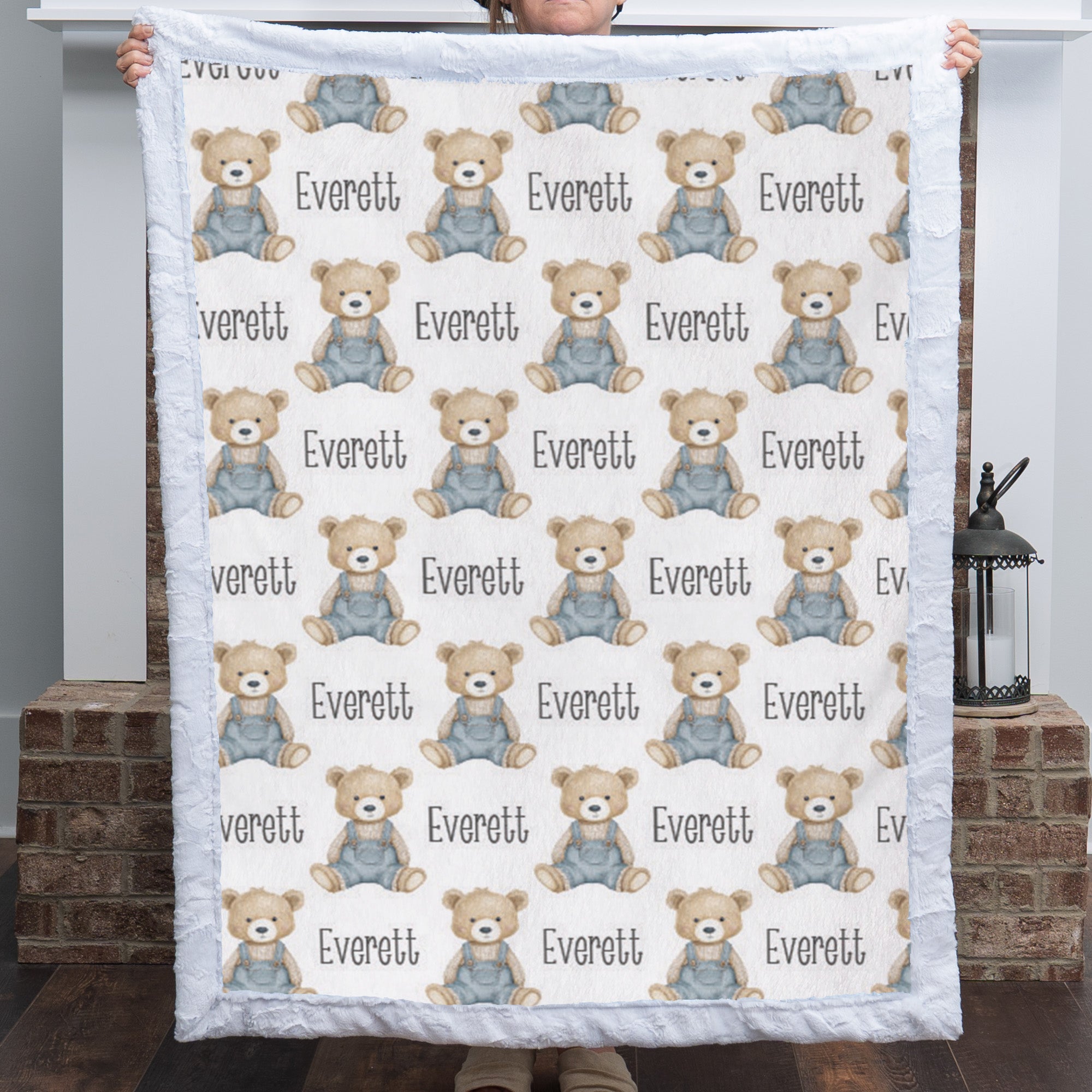 Personalized teddy bear minky baby blanket with white fur border held up by fireplace with lantern