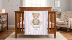 Personalized minky teddy bear baby blanket with pink stripe border draped over wooden crib