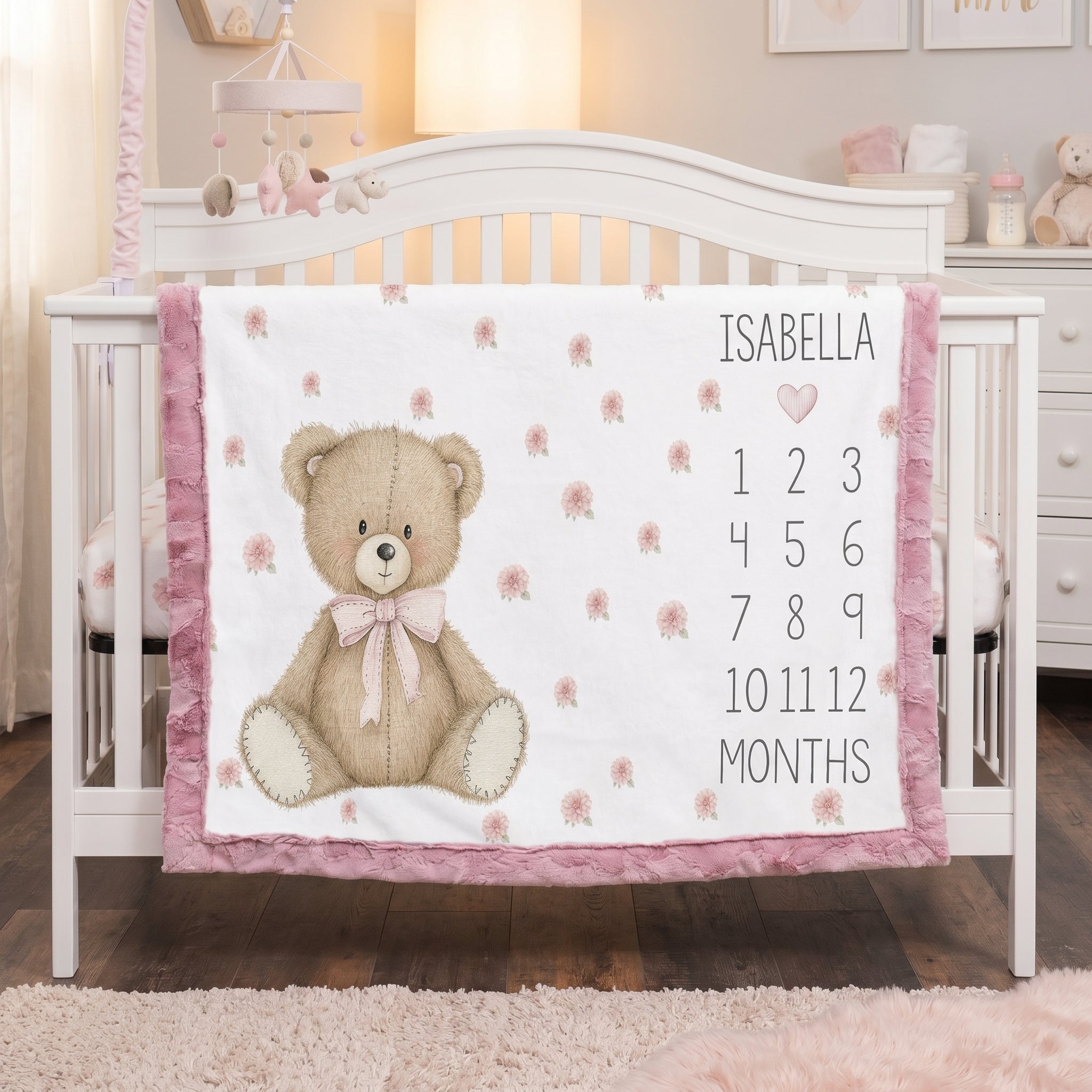 Personalized teddy bear milestone blanket with pink minky trim draped over white nursery crib