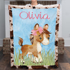 Personalized western pony minky baby blanket with cowhide border and custom name, held up indoors