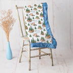 Personalized woodland animal minky blanket with blue trim draped over vintage chair beside dried flowers