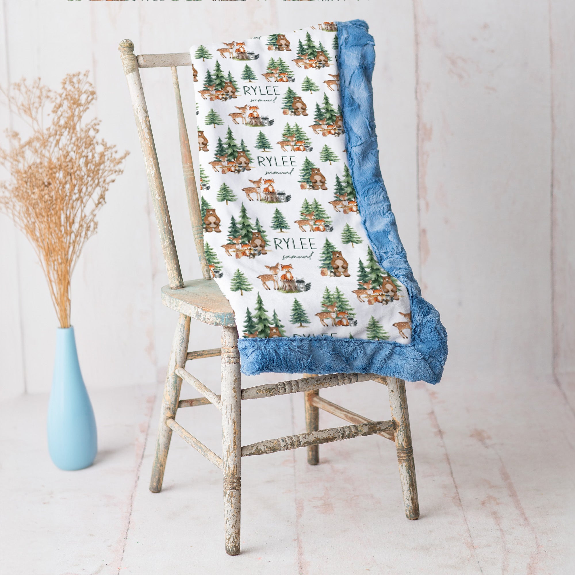 Personalized woodland animal minky blanket with blue trim draped over vintage chair beside dried flowers