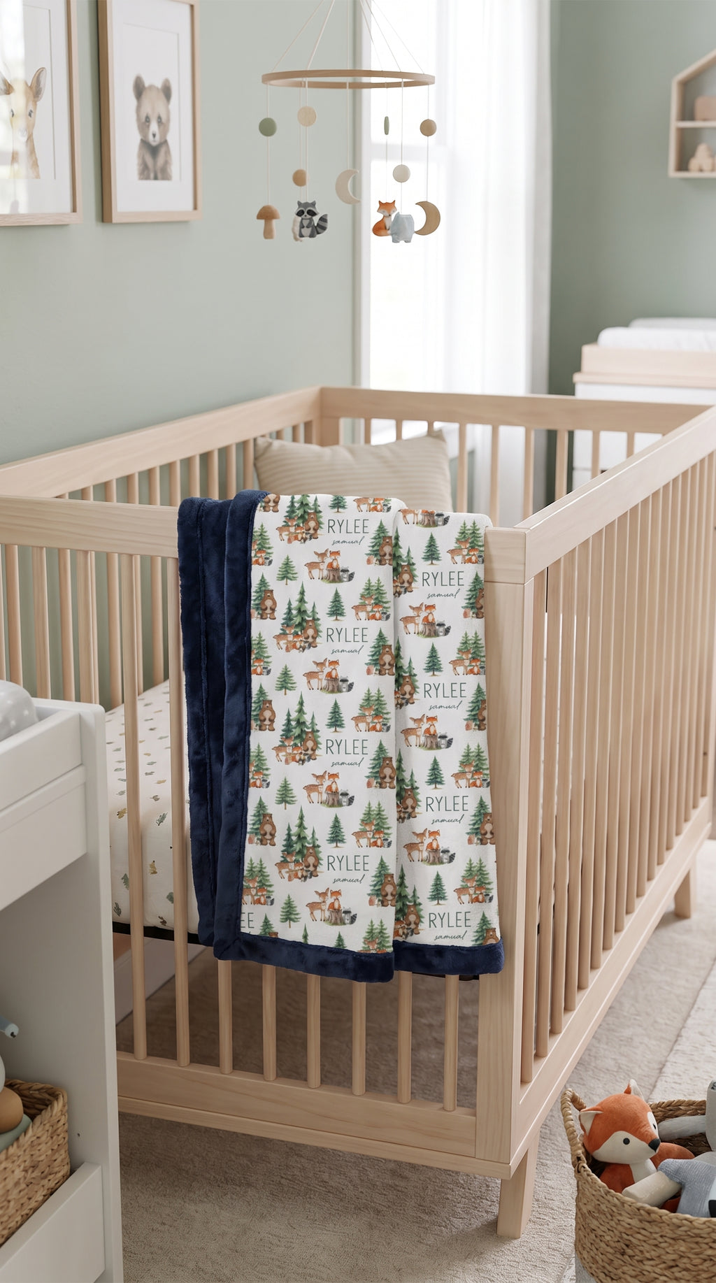 Personalized woodland animal minky blanket with navy trim draped over crib rail in nursery