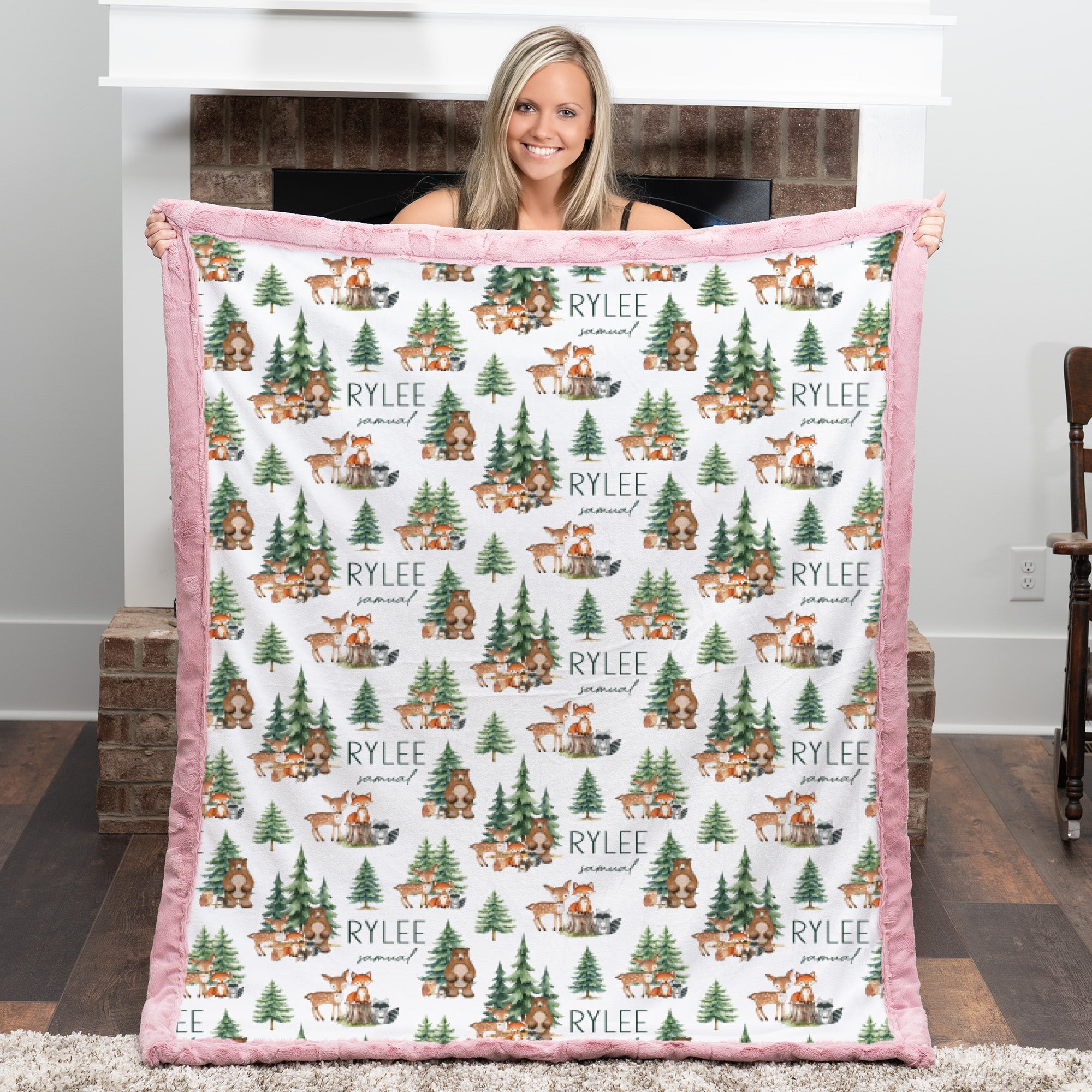 Woman holding personalized woodland animal minky blanket with pink trim over fireplace mantel