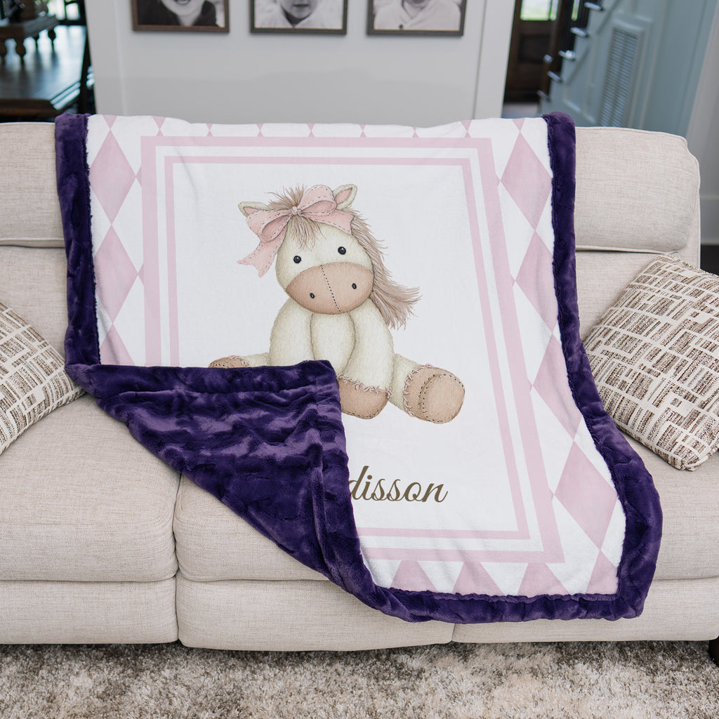 Pink pony minky baby blanket on couch, folded to show plum minky backing