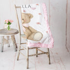 Pink teddy bear floral baby blanket draped over a rustic wooden chair beside a vase of pink roses
