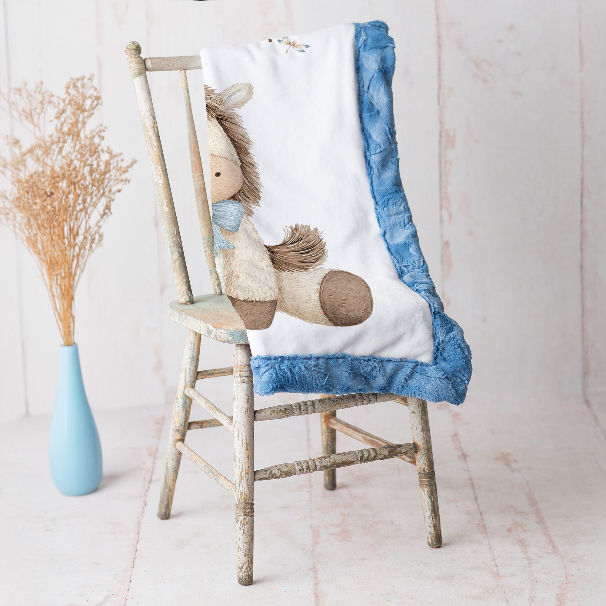 Pony baby blanket with blue minky trim draped over vintage rustic chair
