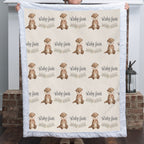 A person holds up a quilted blanket featuring a repeating pattern of brown otters and the text 'Ruby Jane' on a cream background, with a white ruffled border. The background shows a home interior with a brick hearth and a lantern.