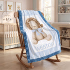 A personalized baby blanket draped over a wooden rocking chair in a nursery. The blanket features a large teddy bear design with the name 'Weston' printed below it, set against a background of light blue and white stripes with a blue plush border.