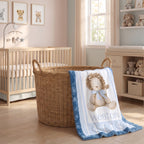 A personalized baby blanket with a blue ruffled border and a teddy bear illustration is draped over a wicker basket in a softly decorated nursery. The blanket features the name 'Weston' printed in blue text.