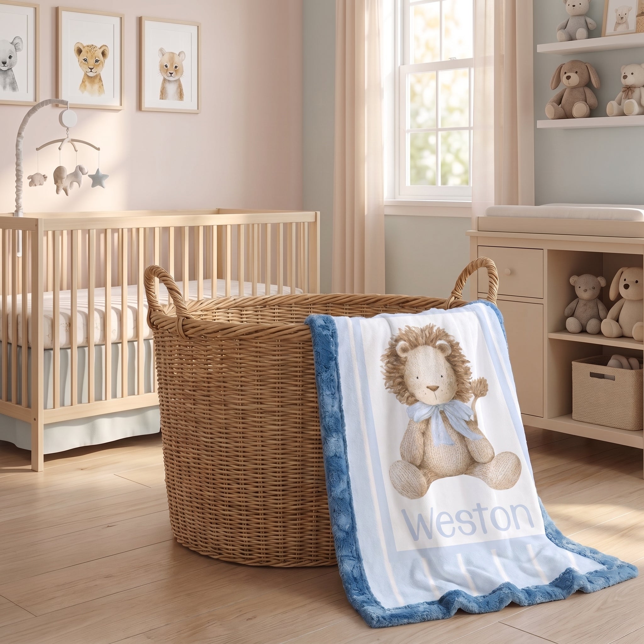 A personalized baby blanket with a blue ruffled border and a teddy bear illustration is draped over a wicker basket in a softly decorated nursery. The blanket features the name 'Weston' printed in blue text.