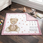 Teddy bear milestone blanket with pink minky trim flat-laid on floor with nursery toys