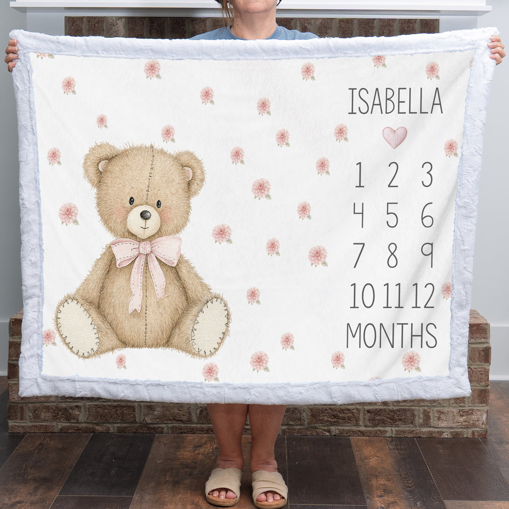 Woman holding teddy bear milestone blanket with white minky trim in front of fireplace mantel