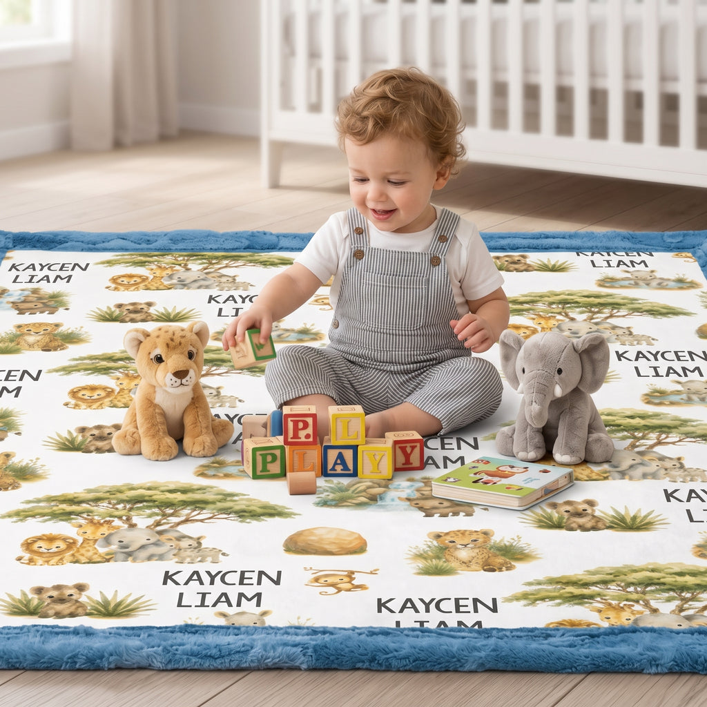A toddler sits cross-legged on a safari-themed baby play mat in a bright nursery, surrounded by plush toys and colorful building blocks. The play mat features illustrated animals and the name 'KAYSEN LIAM'.