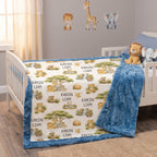 A children's bedding set displayed on a white wooden toddler bed in a nursery. The set includes a plush blue blanket and a matching comforter printed with safari animal illustrations like lions, giraffes, and elephants, along with the personalized name 'KAYSEN LIAM'.