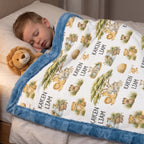 A child sleeping in bed under a white blanket printed with cartoon animals and the names 'KAYEN LIAM', with a blue plush border. A teddy bear toy rests beside the child on the bed.