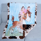 Blanket with a horse design featuring a pink bow on a gray couch.