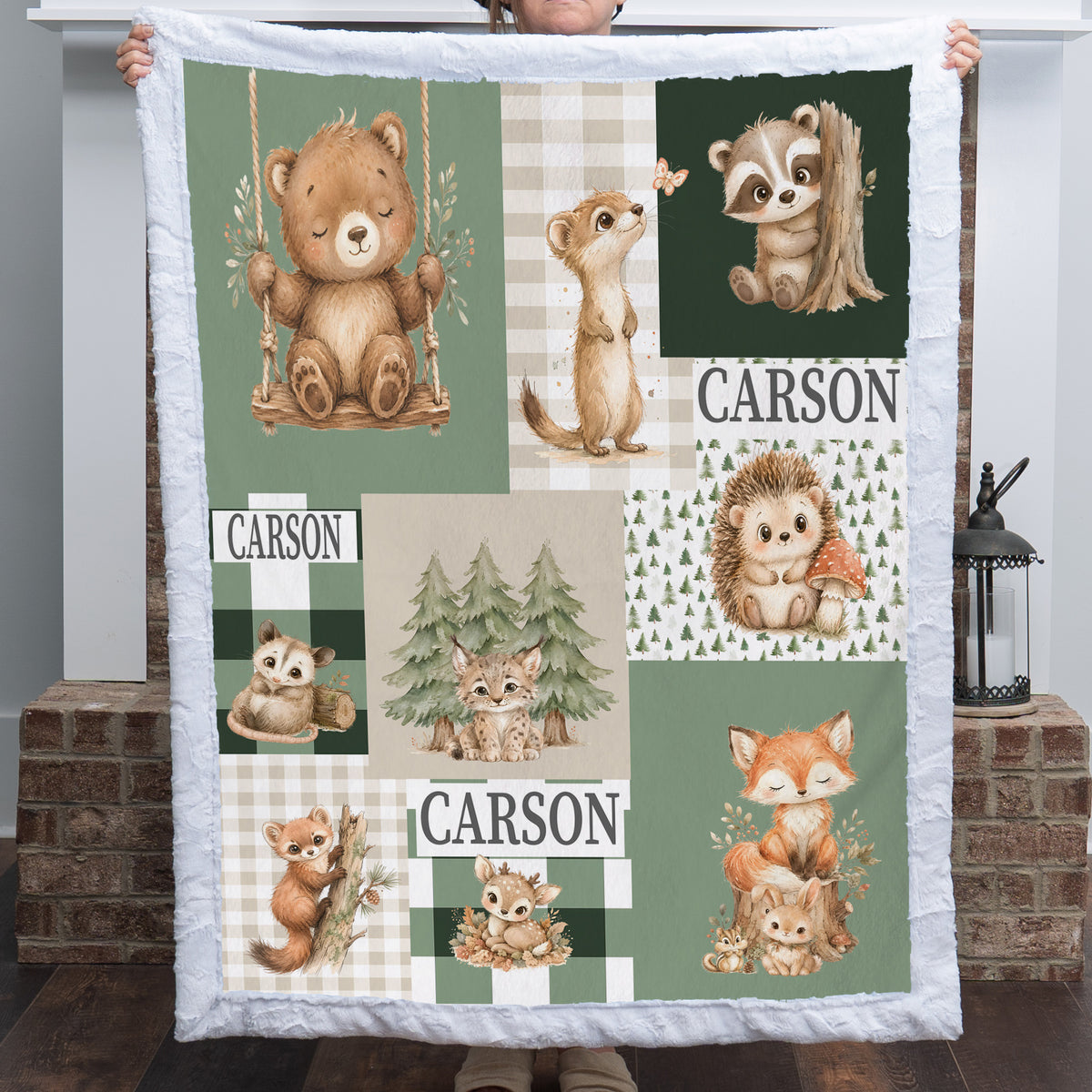 A custom quilted blanket featuring woodland animal illustrations and the name 'CARSON' printed in multiple patchwork panels, held up by a person in front of a brick fireplace.