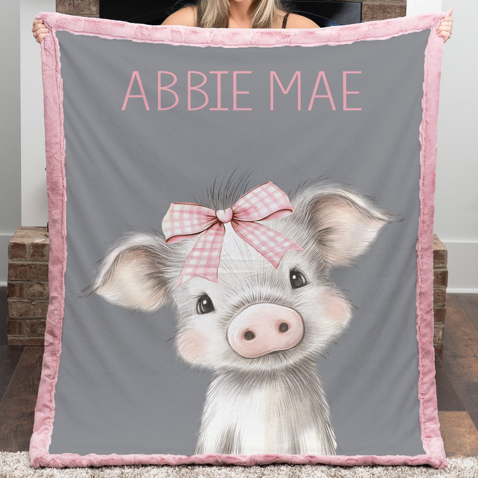 Person holding a gray blanket with a pig illustration and 'ABBBIE MAE' text.