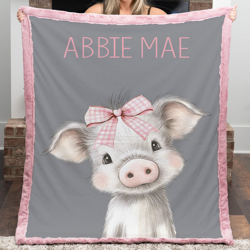 Person holding a gray blanket with a pig illustration and 'ABBBIE MAE' text.